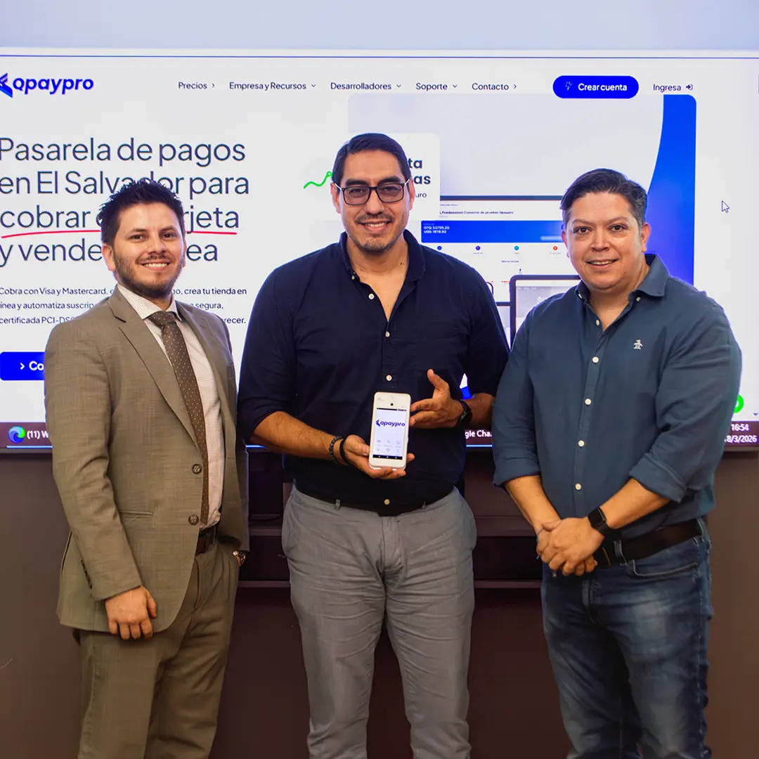 Tres representantes de Qpaypro muestran la aplicación de cobro frente a la pantalla con la pasarela de pagos de Qpaypro El Salvador
