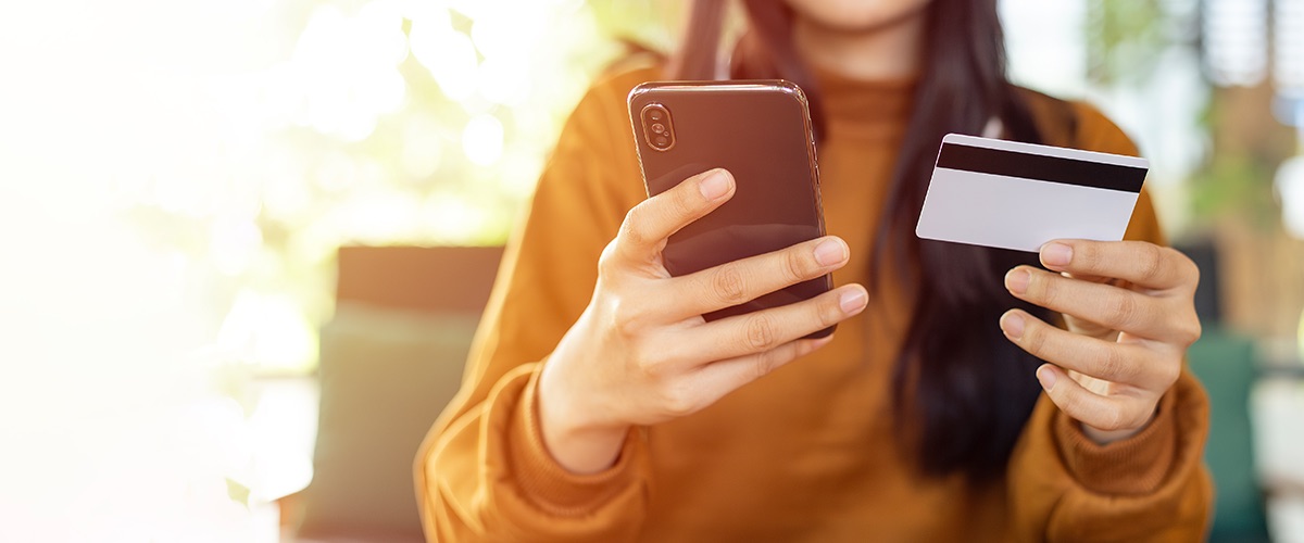 Persona con el teléfono en una mano y la tarjeta en la otra, a punto de pagar